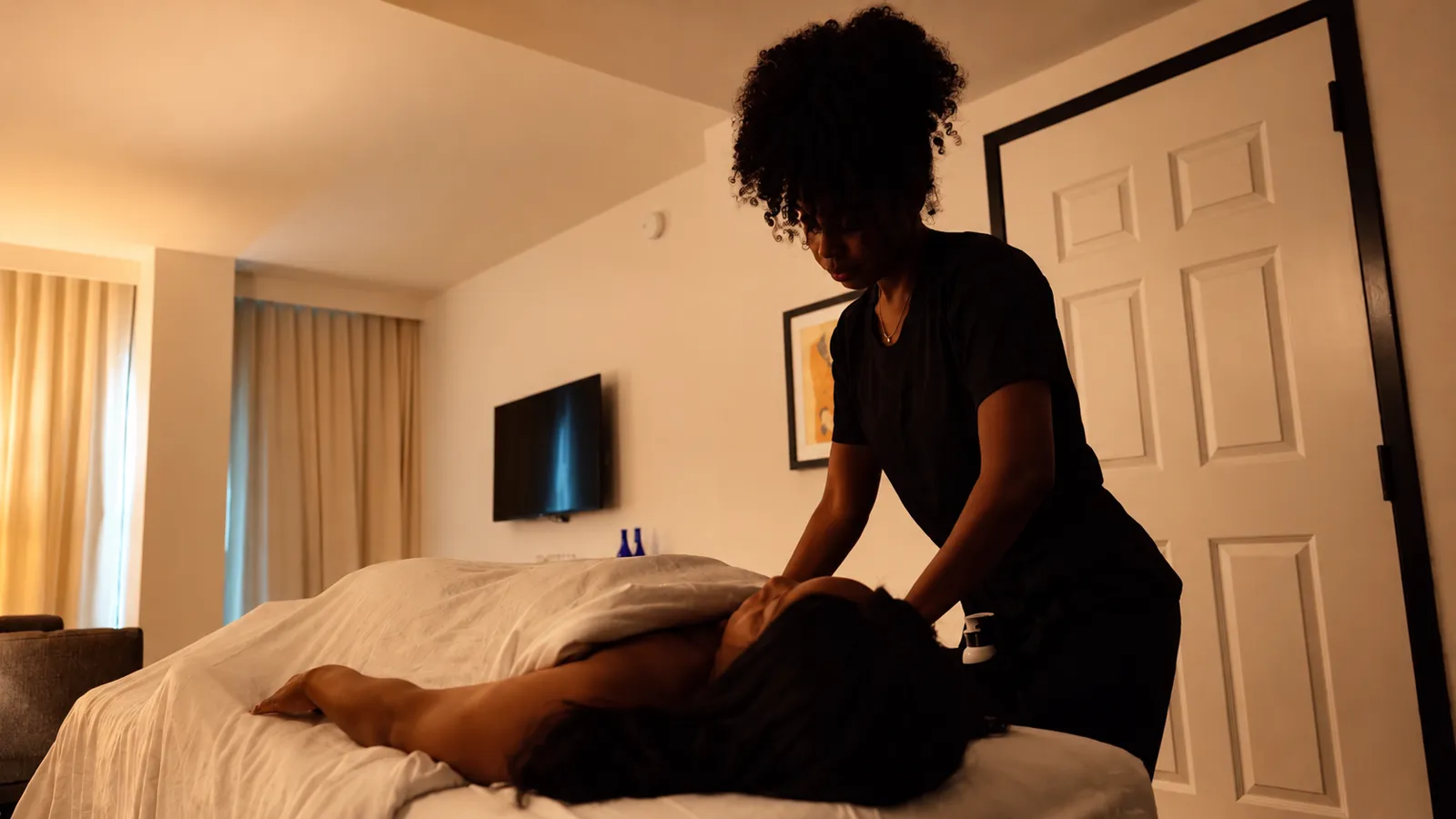 A Peace of Serenity therapist massaging a client’s shoulders on a massage table in a bedroom